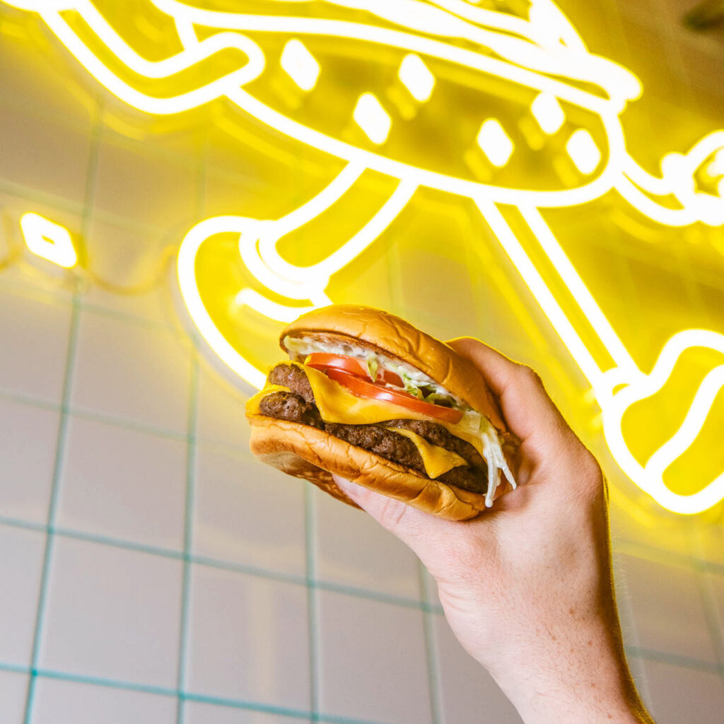 swanky burger held in front of neon sign